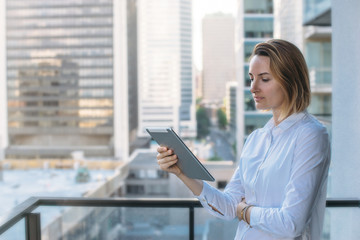 Portrait of young beautiful businesswoman in white shirt using modern tablet outdoors, Tablet on city background, Flare light, Shallow DOF.