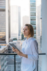 Attractive businesswoman wearing white shirt working on new project of office buildings, manager using modern tablet outside, Tablet on city background, Flare light, Shallow DOF.
