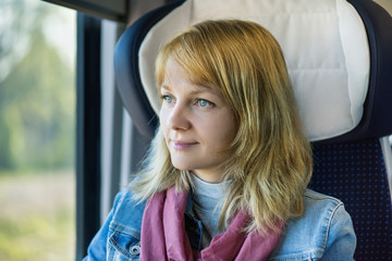 Young pretty woman traveler sitting by train or bus, looking through window