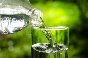 Drink water pouring in to glass over sunlight and natural green background