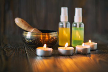 Burning candles and oil for aromatherapy and massage. Singing bowl on dark wooden background.
