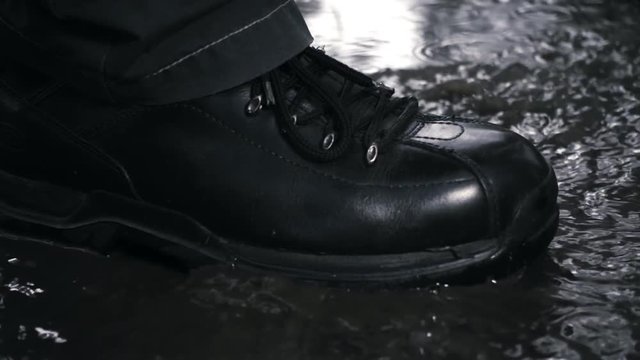 Black new and glossy boots step on a puddle and creates a splash water and dirt which fly around. Slow motion, high speed camera, 250fps