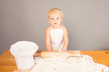 Beautiful blonde boy with big blue eyes knead the dough from flour to bake a delicious cake