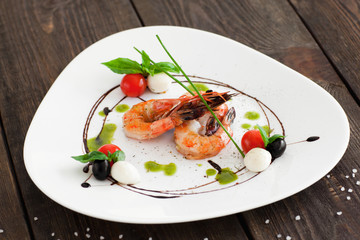 Grilled shrimps on white triangle plate on wooden background, served with olives, cherry tomato and mozzarella cheese