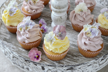 Purple and yellow cupcakes with sugared edible flowers on vintage cake stand