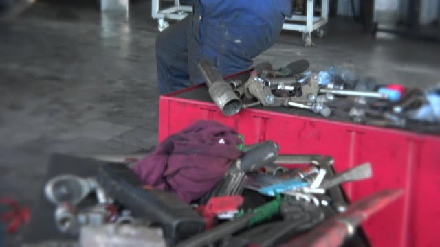 mechanic repairing a car in his garage and various tools on box. Tilt down.