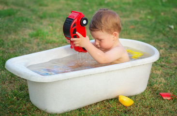 A small baby bathed in the bath and playing with toy car.