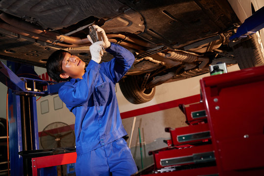 Vietnamese Mechanic Examining Lifted Car In Garage