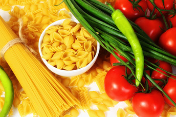 Different types of raw Italian pasta with tomatoes and other vegetables. Top view background.