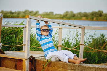 beautiful boy posing sitting on a wooden bridge . Dressed in a nautical theme .