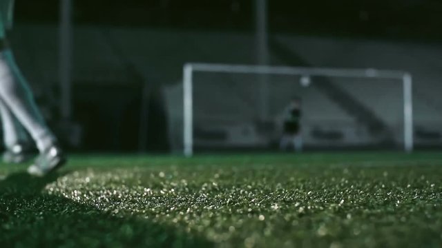 Low angle view of feet of soccer player kicking wet ball on misty grass in the night stadium in slow motion