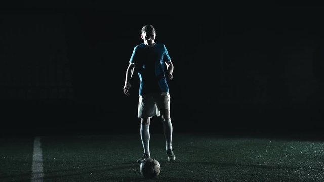 Young sportsman placing a soccer ball and then running and kicking it in slow motion on stadium field in the night