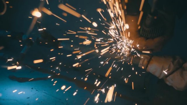 The angular grinding machine is cutting the pipe on a blue background and a lot of sparks flying straight into the camera. Slow motion, high speed camera, 250fps