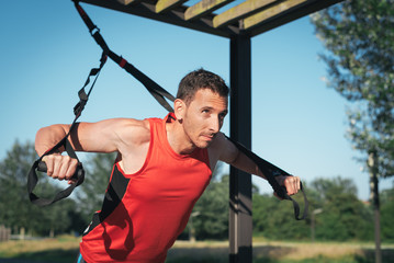 Man doing push ups training arms with trx fitness straps outdoor. Workout healthy lifestyle concept.