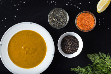 Cream soup of assorted lentil. Yellow and green lens, spices as raw for meal and lemon on black background. Healthy, appetizing, delicious, vegetarian food. Top view, copy space.
