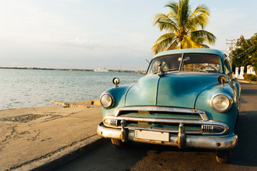 Plakaty  Zabytkowy samochód na plaży na Kubie jako tło.