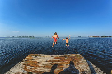 The children, a boy and a girl jumping from a wooden pier in the water.