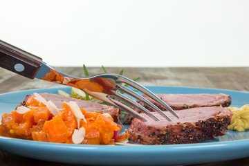 Schweinefilet im Speckmantel, serviert auf blauem Teller mit Karottengemüse. Garniert mit...