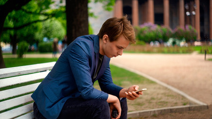 Young businessman sitting on a bench using his cell phone