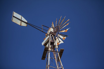 Fototapeta na wymiar Disused rusty old farm windmill against blue sky