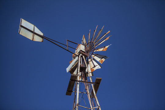 Disused rusty old farm windmill against blue sky