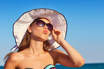 Air kiss from sea. Tanned girl in a hat and sunglasses on the be