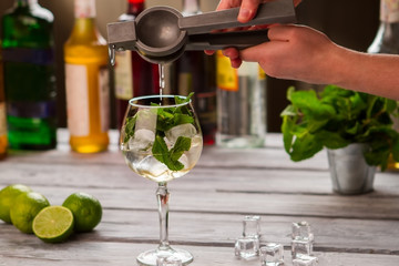 Hands holding lime squeezer. Liquid drips into wineglass. Fresh juice for hugo cocktail. Elderflower syrup and mint.