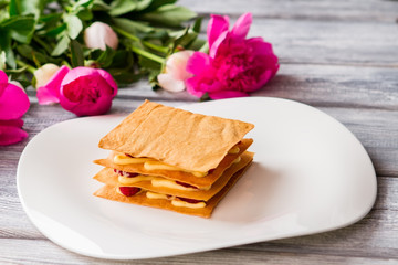 Puff with custard on plate. Bright pink flowers. Raspberry millefeuille served at restaurant. Sweet dish for a gourmet.