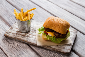 Burger and bucket of fries. Hamburger on piece of paper. Delicious fast food meal. Traditional recipe of beefburger.