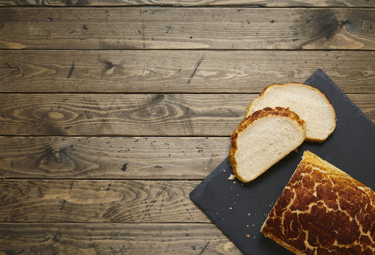 A loaf and slices of crusty white tiger bread on a rustic slate and wooden table top background forming a food themed page border