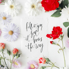 inspirational quote "follow your soul it knows the way" written in calligraphy style on paper with pink, red roses, chamomiles and leaves isolated on white background. Flat lay, top view