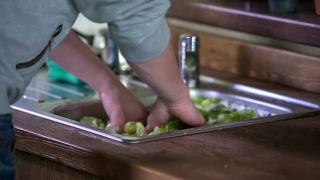 A young man is washing lettuce in the kitchen sink. He will make some salad for himself and his girlfriend. Close-up shot.
