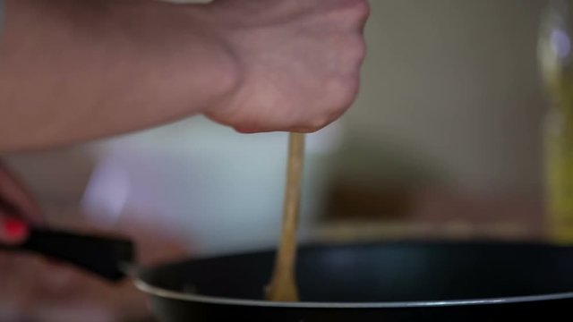 A young man is stirring vegetables in the wok. He is making a meat dish for dinner. Close-up shot.
