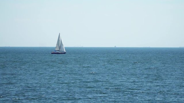 The yacht is under sail floats in the sea. On the horizon are seen cargo ships