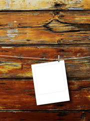 Close-up of one blank instant square photo frame hanged by peg against brown weathered wooden boards background