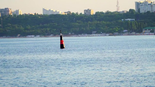 Red-black buoy in sea water as safety warning . Shooting with the ship sailing. Wieden The city on the shore