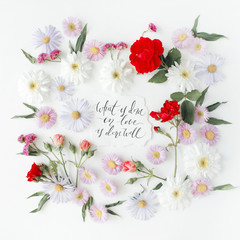 inspirational quote "what is done in love is done well" written in calligraphy style on paper with pink, red roses, chamomiles and leaves isolated on white background. Flat lay, top view