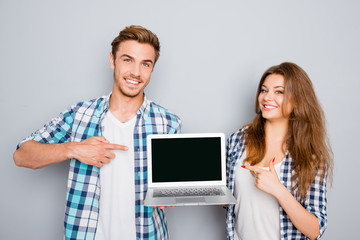Young couple demonstrating laptop and pointing on screen with co