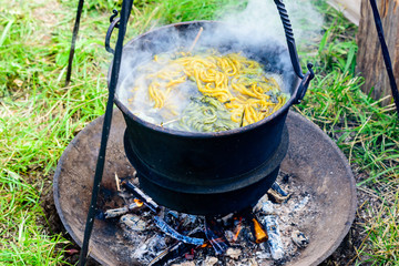 Outdoor hand dying of yarn in an iron pot boiling over open fire. Yarn and herbs present in the boiling water.