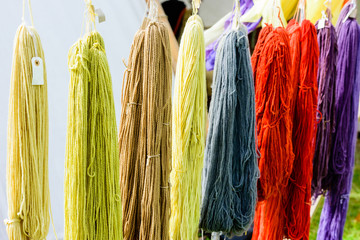 Hand dyed yarn hanging from ropes with white tent in background.