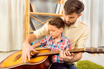 Young father teaching his little son to play on guitar