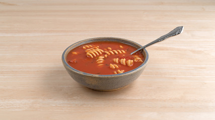 Rotini tomato soup in bowl with spoon on a table.