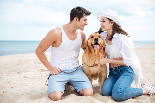 Cheerful couple sitting on the beach with dog