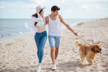 Young couple running along the beach with their dog