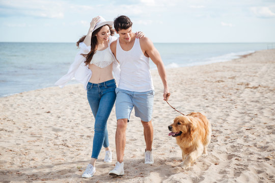 Young Couple Running Along The Beach With Their Dog