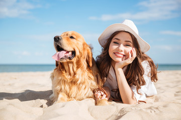 Cheerful young woman lying with her dog on the beach