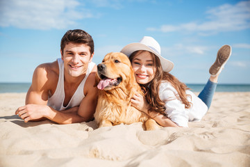 Happy young couple hugging with dog on the beach