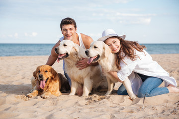 Couple hugging three dogs and sitting on the beach