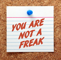 The words You Are Not A Freak in red text on a note card pinned to a cork notice board as a reminder that you are a person and deserve respect
