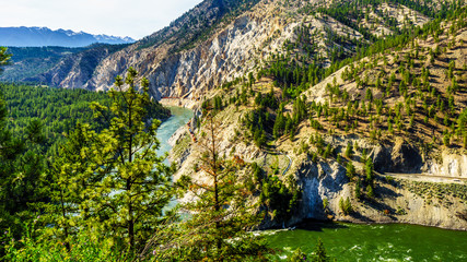 Fototapeta na wymiar Long Container Trains following the Thompson River along steep Cliffs and through Tunnels in the Fraser Canyon in British Columbia